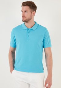 Camisa polo turquesa hecha de tejido texturizado, con un cuello clásico, tapeta de tres botones y mangas cortas.