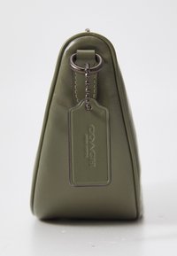 Borsa in pelle verde a forma triangolare, con un anello di metallo e un'etichetta che mostra il logo "COACH". Texture liscia con dettagli di cucitura.