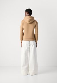 Felpa beige con cappuccio dal tessuto morbido, polsini aderenti e pantaloni abbinati di un bianco puro, caratterizzati da una gamba ampia e ampie tasche.