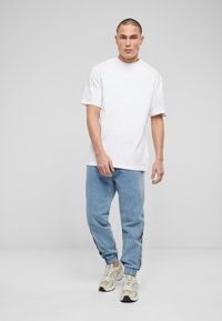 Tricou alb din bumbac, cu mâneci scurte, asociat cu pantaloni jogger din denim albastru cu manșete. Încălțămintea constă în adidași bej cu accente și șireturi negre.