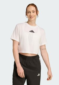 T-shirt blanc court avec le logo Adidas sur la poitrine, associé à un pantalon de sport noir avec des rayures blanches et le logo sur la cuisse.