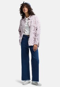 Jasnofioletowa kurtka z kordurojowej tkaniny z teksturowanym nadrukiem w leoparda, zestawiona z wysokim stanem niebieskimi dżinsowymi spodniami rozszerzającymi się na dole oraz białymi trampkami.