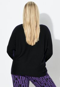 Czarny sweter o luźnym kroju z fioletowymi akcentami na ramionach, zestawiony z fioletowymi legginsami w wzory z tekstowym nadrukiem.