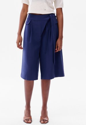 Navy blue culottes made from lightweight fabric, featuring a high waist, side pockets, a tie belt, and a loose, flowing silhouette.