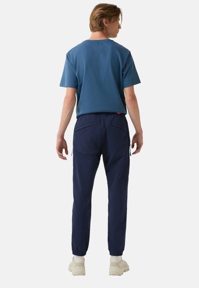 Blaues Baumwoll-T-Shirt mit kurzen Ärmeln, kombiniert mit marineblauen Hosen mit elastischem Bund, die seitliche Reißverschlüsse und schräge Taschen haben.
