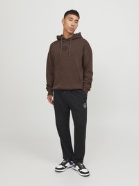 Sudadera marrón con cordón y bolsillo frontal, combinada con pantalones de chándal negros con un logo, y zapatillas negras y blancas.