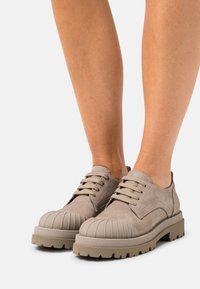 Scarpe in suede beige con punta arrotondata e scanalata, suole spesse e testurizzate, e lacci a contrasto, progettate per durabilità e comfort.