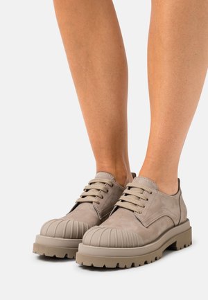 Scarpe in suede beige con punta arrotondata e scanalata, suole spesse e testurizzate, e lacci a contrasto, progettate per durabilità e comfort.