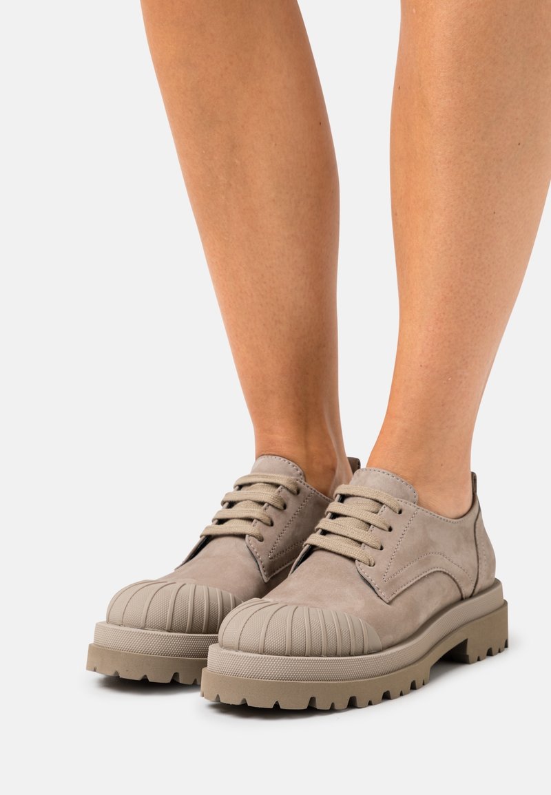 Scarpe in suede beige con punta arrotondata e scanalata, suole spesse e testurizzate, e lacci a contrasto, progettate per durabilità e comfort.