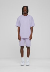 Hellblau oversized T-Shirt und passende Shorts, aus Baumwollmischung gefertigt. Das Modell trägt weiße Sneakers und Knöchelsocken. Schlichtes Design und weiche Textur.