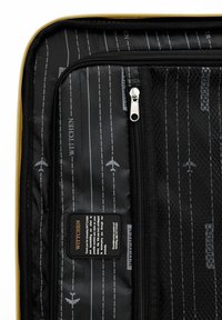 Zwarte kofferinterieur met een gaas ritsvak, vliegtuiggraphics en een gestreept patroon. Een gele ritssluiting accentueert de tas.