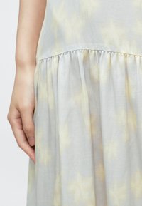 Lysegrå stofkjole med en indsnøret talje og bløde, diskrete gule blomsterprint, lavet af et glat, let materiale.