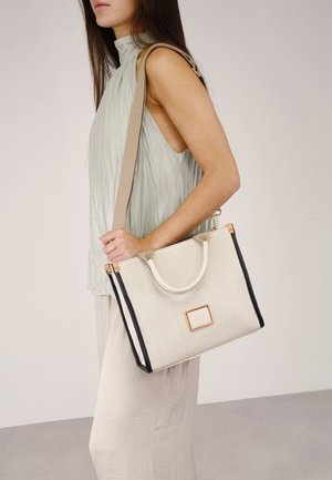Bolso de mano texturizado beige con acentos negros, de forma estructurada y doble asa. Presenta una etiqueta rectangular con un marco dorado.