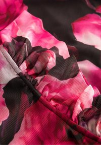 Tkanina w kwiaty z różowymi różami na czarnym tle, z teksturowaną powierzchnią i marszczeniami wzdłuż szwu.