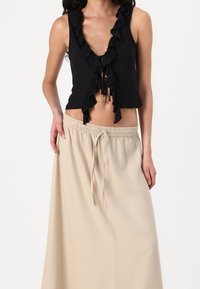 Top corto negro con volantes y escote en V profundo, combinado con una falda larga beige con cordón hecha de una tela ligera.