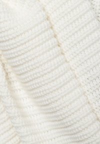 Couverture tricotée blanche présentant un motif texturé avec des lignes en relief et une apparence douce et confortable. Le matériau semble être basé sur du fil.