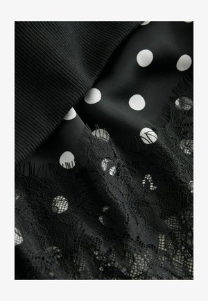 Sort stof med hvide polkaprikker lagdelt over blonder. Har en struktureret, ribbet top og indviklet, blomsteragtig blonde detaljering langs kanten.
