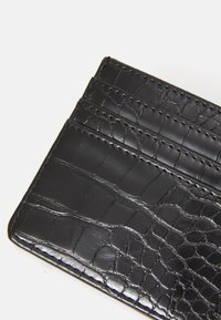 Portacarte in pelle con motivo coccodrillo nero, dotato di quattro scomparti per carte cuciti, su sfondo bianco.