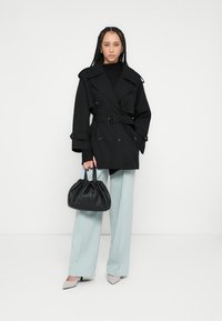 Czarny dwurzędowy trencz z paskiem, zestawiony z jasnoniebieskimi szerokimi spodniami oraz czarną skórzaną torebką na sznurek.