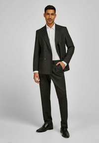 Donker gestreept pak met een dubbelgeknoopte jas en slim-fit broek, gecombineerd met een wit overhemden en zwarte schoenen. Glad oppervlak.