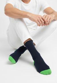 Temno modre nogavice z zelenimi poudarki na prstu in peti. Iz mehkega, raztegljivega materiala. Prilegajo se tesno in so zasnovane za udobje.