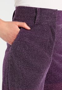 Purple glittery pants with a textured fabric, featuring a side pocket and a high waistband. The sparkle adds a distinctive detail.