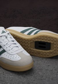 Weiße Sneakers mit grünen Streifen, Wildleder-Spitzenschutz, perforierte Details und einer Sohle aus Gummi mit Fischgrätmuster.