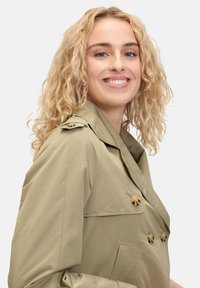 Licht kaki trenchcoat met een dubbelzijdig ontwerp, gouden knopen en een wijde kraag, gemaakt van een gladde, lichte stof.