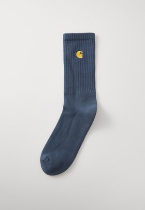 Marineblaue, gerippte Socken aus einem weichen Stoff, mit einem kleinen gelben Logo nahe dem Bund. Glatte Textur mit verstärkter Zehenpartie.