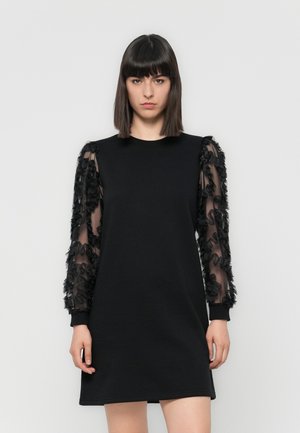 Robe noire avec un corps uni et des manches transparentes ornées d'accents en tissu noir froncé. Encolure ronde et manches longues, design arrivant au genou.
