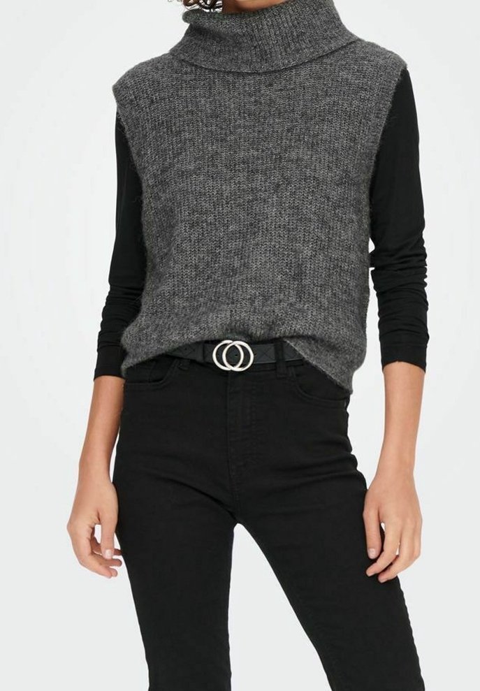 Personne portant un pull à col roulé gris sans manches par-dessus une chemise noire à manches longues, associé à un pantalon noir taille haute et une ceinture avec boucle à anneau double.
