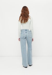 Jean large bleu clair à taille haute, avec un design de poche arrière simple et une ceinture unie. Texture de denim lisse.