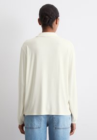Langermet kremfarget bluse i et glatt, lett stoff, med krage og avslappet passform, kombinert med lys blå denimjeans.