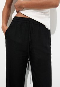 Pantalones negros con cordón y corte relajado, confeccionados con tejido ligero. Cuentan con bolsillos laterales y una textura lisa, adecuados para un uso casual.