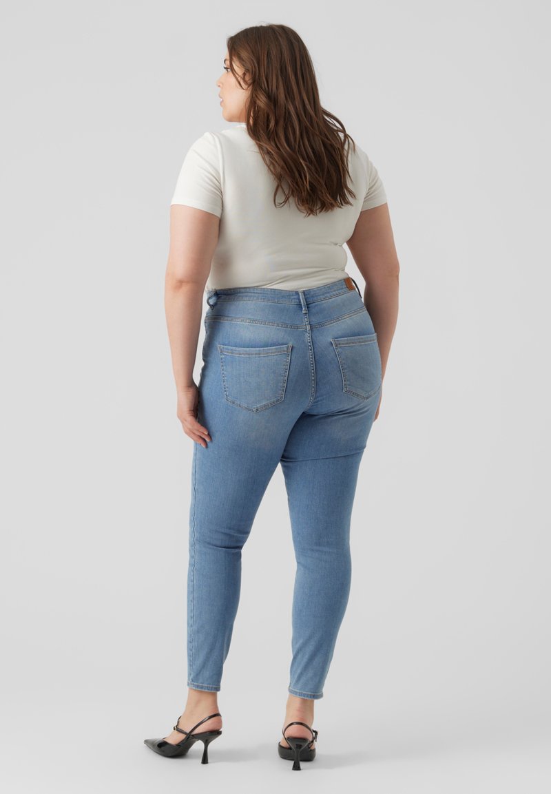 Lyseblå skinny jeans med høy midje, to baklommer og en glatt tekstur, kombinert med en hvit tettsittende topp og svarte stroppestiletter.