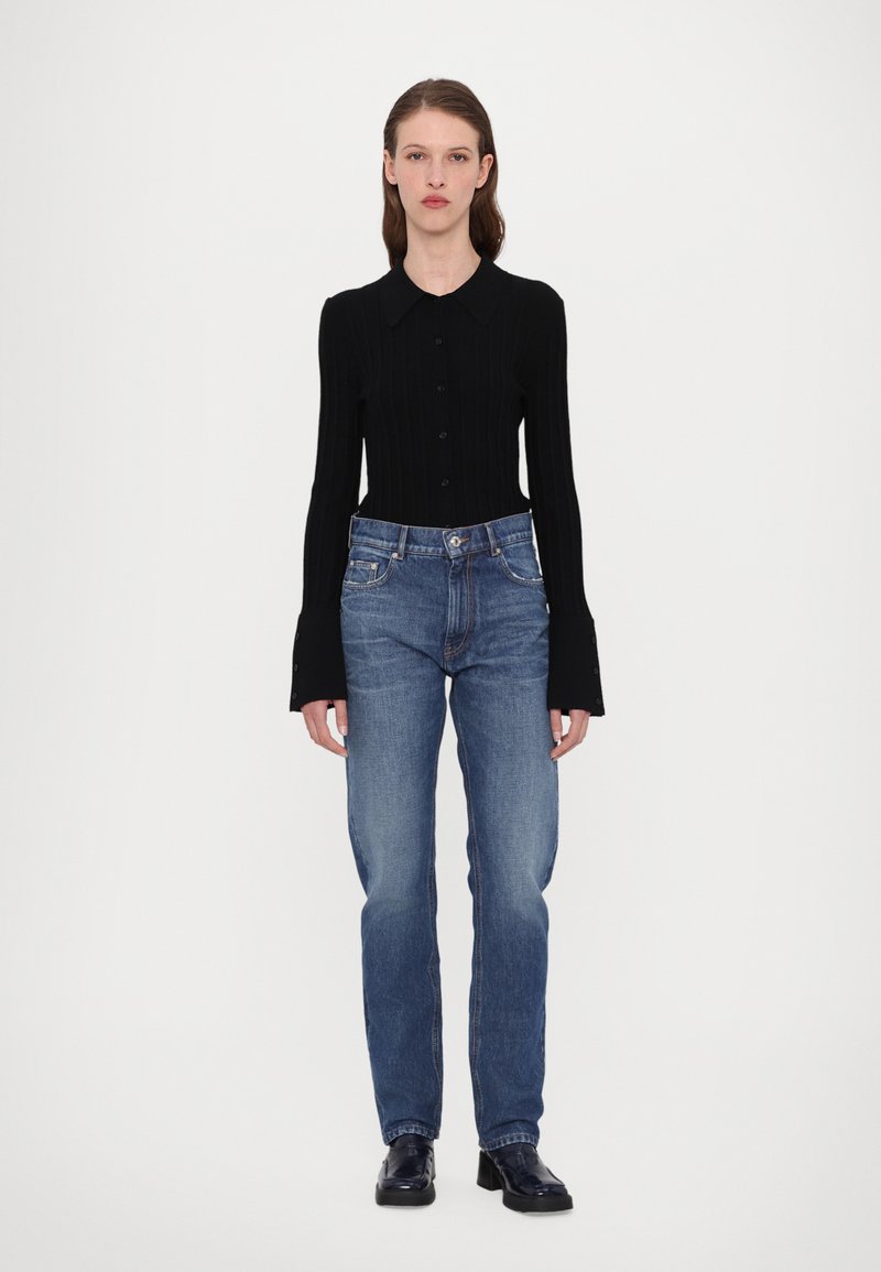 Haut noir à manches longues côtelé avec un col. Assorti à un jean bleu moyen et des chaussures noires. Design simple, silhouette ajustée.