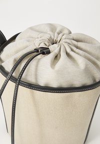 Geantă tip bucket cu un corp dintr-un material bej texturat, cu partea de sus strânsă, și accente din piele neagră. Dispune de șnururi cu cusături de contrast.