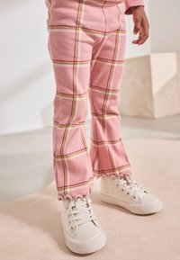 Pantaloni rosa in velluto a coste con motivo a quadri, con linee gialle e bianche, gambe svasate e orlo smerlato, abbinati a sneakers bianche.