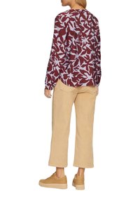 Langarmshirt in bordeauxrood met een lichtblauw bloemenpatroon, gecombineerd met beige corduroypants en tan platform sneakers.