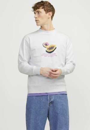 Grå sweatshirt med et farverigt grafik af en delt passionsfrugt. Ribbet halsudskæring og manchetter, iført over en lilla skjorte, parret med blå jeans.