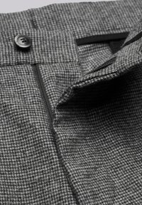 Gray patterned fabric with a houndstooth design, featuring a button closure and zipper detail. The texture appears soft and woven.