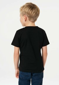 Black short-sleeve t-shirt made of cotton, features a round neckline and is paired with blue corduroy pants. Visible stitching on sleeves.