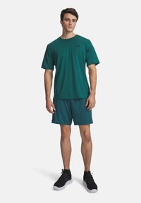 Τυρκουάζ αθλητική μπλούζα με κοντά μανίκια, συνδυασμένη με τυρκουάζ σορτς. Η εμφάνιση ολοκληρώνεται με μαύρα αθλητικά παπούτσια και έχει ένα διακριτικό λογότυπο.