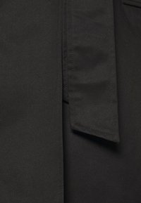 Tessuto nero con una texture liscia, caratterizzato da un ampio colletto e cuciture. Include un lungo nastro che si estende dalla scollatura.