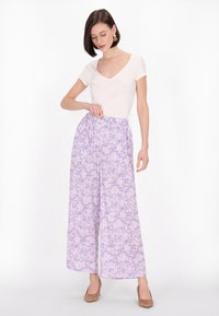 Paarse bloemenpatroonwijdelonten broek met een elastische tailleband, gecombineerd met een aansluitend wit T-shirt met korte mouwen en beige hakken.