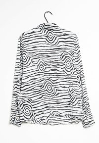 Black and white patterned shirt with a wave design, long sleeves, collared, lightweight fabric, and a slightly curved hem.
