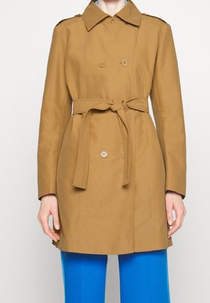 Trench coat marrone doppiopetto con vita regolabile, dotato di due bottoni, colletto e maniche lunghe. Indossato sopra pantaloni blu.
