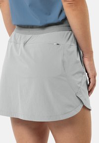 Lichtgrijze sportrok met een gladde textuur, elastische tailleband en een ritszak aan de achterkant. Heeft een afgeronde zoomlijn en zijsplitten.