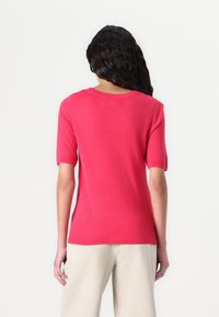 Fitted, short-sleeved top in vibrant pink knit fabric with a scoop neckline and smooth texture, paired with light-colored pants.