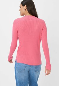 Roze geribbelde trui met lange mouwen en een ronde hals. Beschikt over zijsplitten en een getailleerd ontwerp. Gecombineerd met lichtblauwe jeans.
